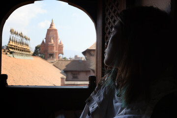 girl watch outside though Newar window window having the view of temple of Silu Mahadeva in...