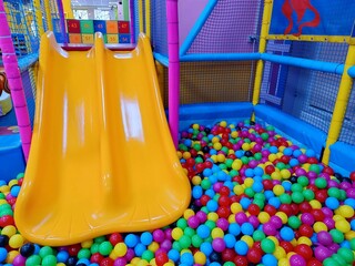 Yellow slide, descent in dry pool with multi-colored plastic balls. Children's playroom, Entertainment center. Labyrinth indoors empty game room in kindergarten. Design interior