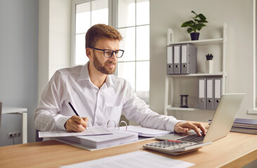 Portrait of young attractive business man wearing white shirt working at the desk with a pile of...