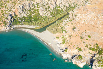 The sandy beach at the foot of the mountain next to a green palm grove , in Europe, Greece, Crete, Preveli, By the Mediterranean Sea, in summer, on a sunny day.