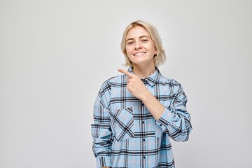 Young blond woman in casual pointing aside finger, demonstrating empty space for product or text...