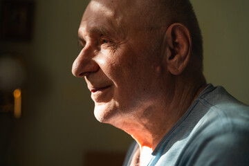 Elderly senior man at home in shadow and sunlight with headache. Retirement medical problems, high...