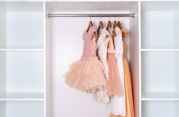 Children's carnival dresses hang on wooden hangers in white closet.