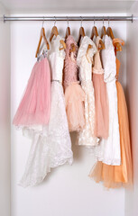 Pink, white and peach puffy dresses hang in a white closet. Clothing storage concept.