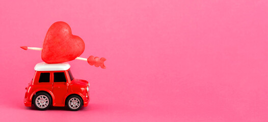 Red retro toy red car with red heart with arrrow for Valentine's day on pink background. Wide...