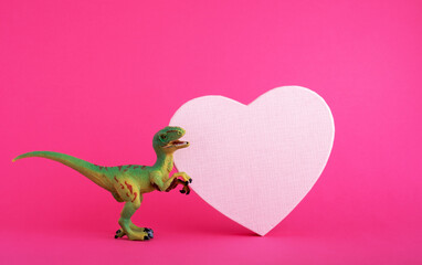 Green cute dinosaur with pink heart on vivid pink background. Creative minimal greeting card on Valentines day. Love concept.
