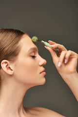 Obraz premium side view of young woman with closed eyes doing face massage with jade roller on grey background