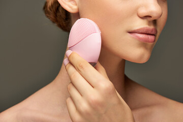 cropped woman holding cleansing brush on grey background, beauty gadget and skin care concept - obrazy, fototapety, plakaty
