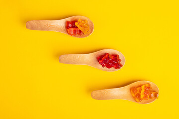 Jelly bears candy in wooden spoon, gummy bear on yellow background