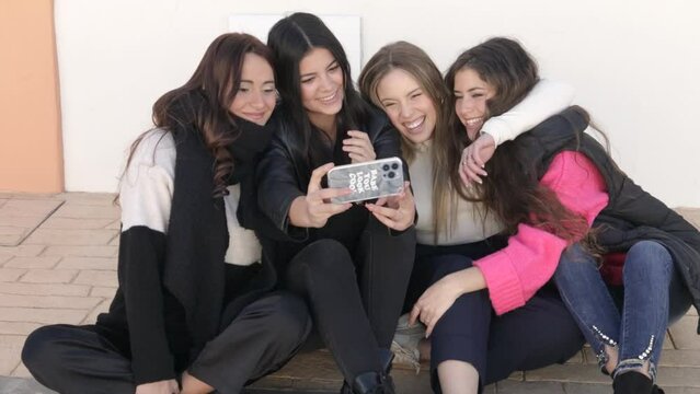 happy female friends sitting together taking photos with a smartphone