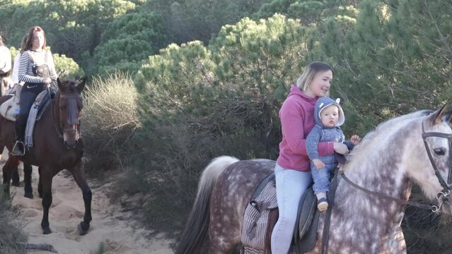 woman with baby and happy friends riding horses in the countryside
