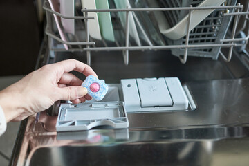 Closeup of woman putting dishwasher detergent into dishwasher machine