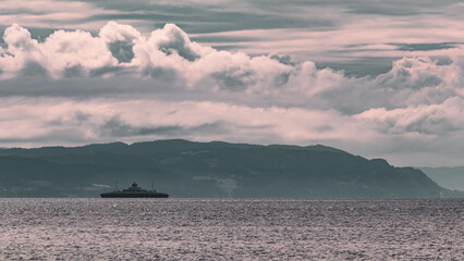 Ship against the background of mountains in the Trondheim fjord. Dramatic clouds before the storm.