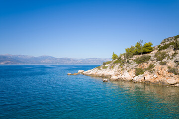 The arid rocky coast and its green countryside along small beaches, in Europe, Greece, Peloponnese, Argolis, Nafplio, Myrto seashore, in summer, on a sunny day.