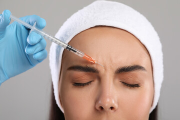 Doctor giving facial injection to young woman on light grey background, closeup. Cosmetic surgery