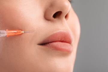 Young woman getting facial injection on light grey background, closeup. Cosmetic surgery