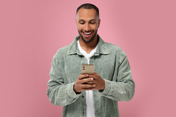Happy man sending message via smartphone on pink background