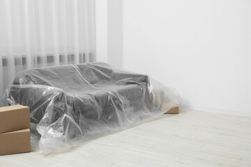 Stylish sofa covered with plastic film and boxes at home. Space for text