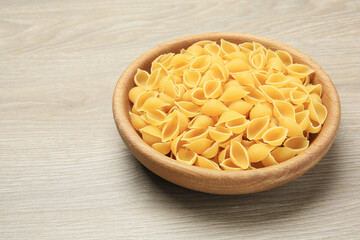 Raw conchiglie pasta in bowl on light grey wooden table, space for text