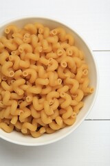 Raw cavatappi pasta in bowl on white wooden table, top view