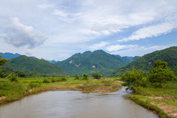 Fototapeta na wymiar A river in the middle of green rice fields and mountains, in Asia, Vietnam, Tonkin, towards Hanoi, Mai Chau, in summer, on a sunny day.