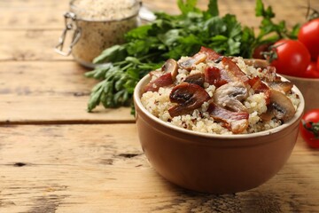 Tasty quinoa porridge with fried bacon and mushrooms in bowl on wooden table, closeup. Space for text