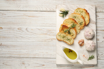 Tasty baguette with garlic, dill, rosemary and oil on white wooden table, top view. Space for text
