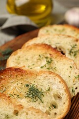 Tasty baguette with garlic and dill on wooden tray, closeup