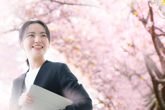 桜の中でパソコンを持つビジネス女性　新卒、新入社員や春の就職のイメージ