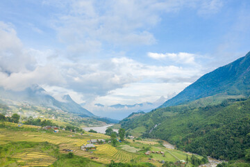 Fototapeta na wymiar The traditional village with green and yellow rice fields in the green mountains, Asia, Vietnam, Tonkin, Sapa, towards Lao Cai, in summer, on a cloudy day.
