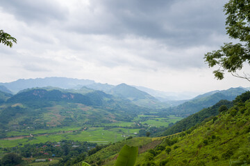 The rice fields and green mountains in the valley, Asia, Vietnam, Tonkin, between Mai Chau and Moc Chau, in summer, on a cloudy day.