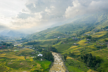 The traditional village with green and yellow rice fields in the green mountains, Asia, Vietnam, Tonkin, Sapa, towards Lao Cai, in summer, on a cloudy day.