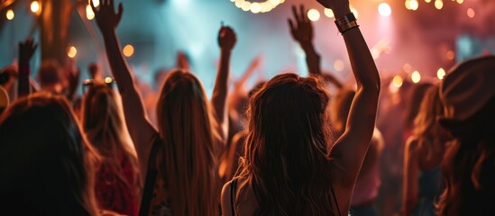 Stylishly dressed girls dancing and raising hands at a modern indoor club concert. - obrazy, fototapety, plakaty