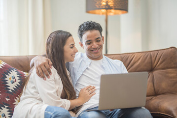 Fototapeta premium Young couple moving to a new home relaxing sitting on the sofa using computer laptop, smiling happy for moving to new apartment