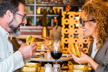 Happy couple smiling and talking in a pub restaurant eating burgers and chips - Married couple having lunch break at cafe bar - Lifestyle concept with man and a woman going out on weekend day