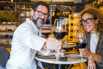 Happy couple smiling and talking in a restaurant drinking red wine - Married couple having lunch break at cafe bar - Lifestyle concept with man and a woman going out on weekend day