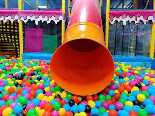 Orange slide red pipe, descent in dry pool with multi-colored plastic balls. Children's tunnel in playroom, Entertainment center. Labyrinth indoors empty game room in kindergarten. Design interior