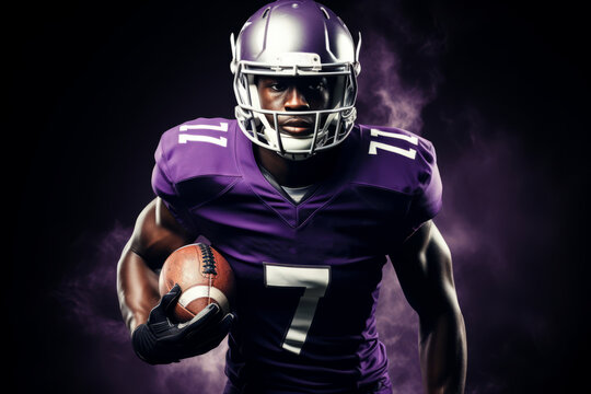 Portrait of American football player running with the ball. Muscular athlete in a purple and yellow uniform with an ovoid ball in a dynamic pose. Isolated on black background.