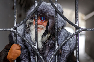 An elderly gray-haired man with a magnificent mustache and beard looks into the distance and smiles. Close-up portrait of an elderly stylish hipster man wearing a fur hat and fur coat. Christmas © Светлана Густова