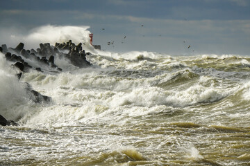Storm at sea, high waves crashing against the concrete breakwaters of the port, white splashes
