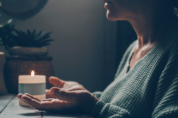Woman at home in zen meditation activity and candlelight in background. One female people with hands up pray or meditate alone in dark light indoor. Concept of healthy mental lifestyle. Nature - obrazy, fototapety, plakaty