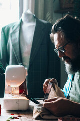Man at home using sewing machine to tailor and modify garments. Blazer in background. Tailoring and...