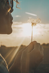 Day dreaming leisure activity with woman blowing a dandelion outdoor in the nature park. Emotion...