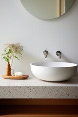 Fototapeta premium Fragment of minimalist bathroom with white wall, Terrazzo stone countertop, white sink, wall mounted faucets and elegant stand for cosmetic accessories.