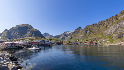 Panoramic view from the water featuring classic red wooden Rorbu houses on the rocky shores of...