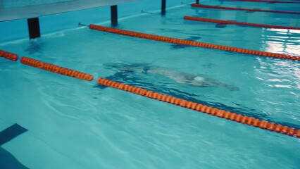 Athlete swimmer man swims, makes a turn under water and continues to swim in the backstroke style. Male swimmer swimming in the indoor pool - Powered by Adobe