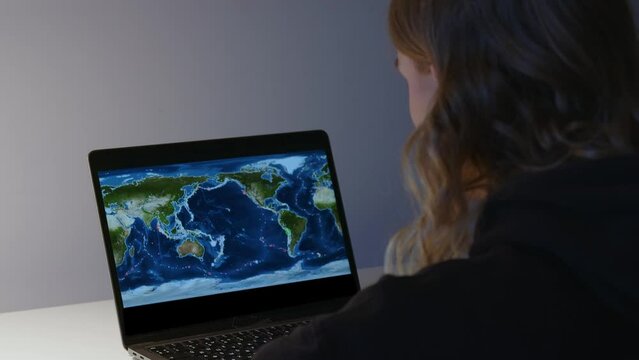 Global Awareness: Girl Monitors Earthquake Activity on World Map. A girl is observing a map displayed on her laptop screen, which seems to show seismic activity or earthquake data across the globe