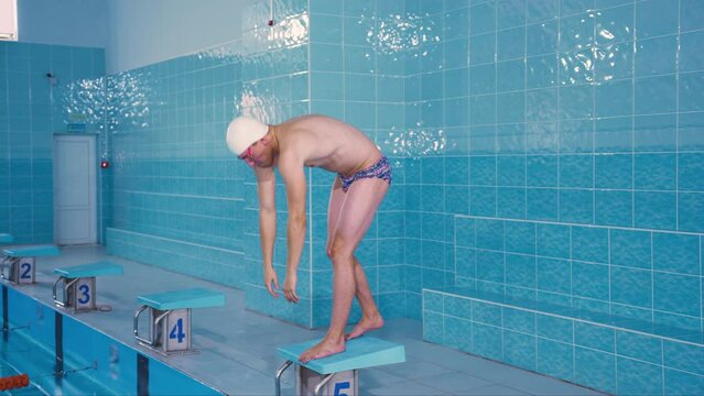 Professional athlete swimmer man preparing to jump into water in a swimming pool. Swimmer training before the championship.