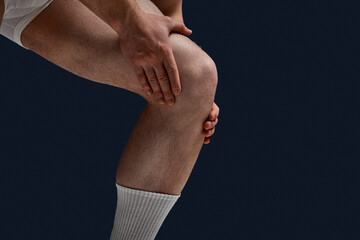 Cropped close up photo of female lag. Man put hand on knee because he feel pain, joints hurt against blue studio background. Concept of men's health, lifestyle, beauty, body and skin care