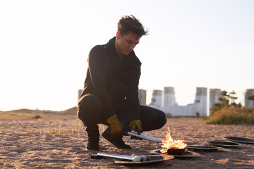 Full length portrait of young man as fire show artist dipping metal torches in fuel liquid on beach...
